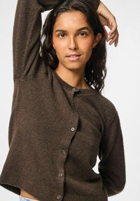 Cardigan a maglia marrone con scollatura rotonda, chiusura a bottoni e tessuto texturizzato. Maniche lunghe con una vestibilità rilassata, che conferiscono un aspetto accogliente.