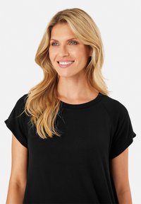 T-shirt noir à manches courtes avec un col rond. Tissu doux, coupe décontractée et manches retroussées. Texture lisse sans motifs visibles.