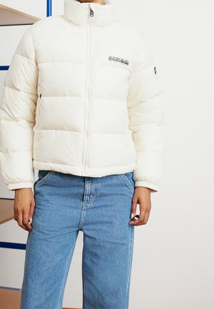 Personne portant une doudoune blanche à fermeture éclair avec le logo Napapijri sur la poitrine, associée à un jean en denim bleu clair.