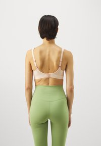 Lys rosa trådløs BH med justerbare stropper, baklukking og glatt tekstur, kombinert med høy midje grønne leggings.
