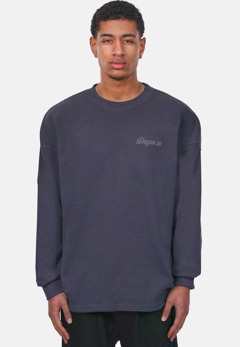 Sudadera de manga larga gris oscuro con textura de gofre, cuello redondo, puños de canalé y un discreto logo bordado en el pecho.