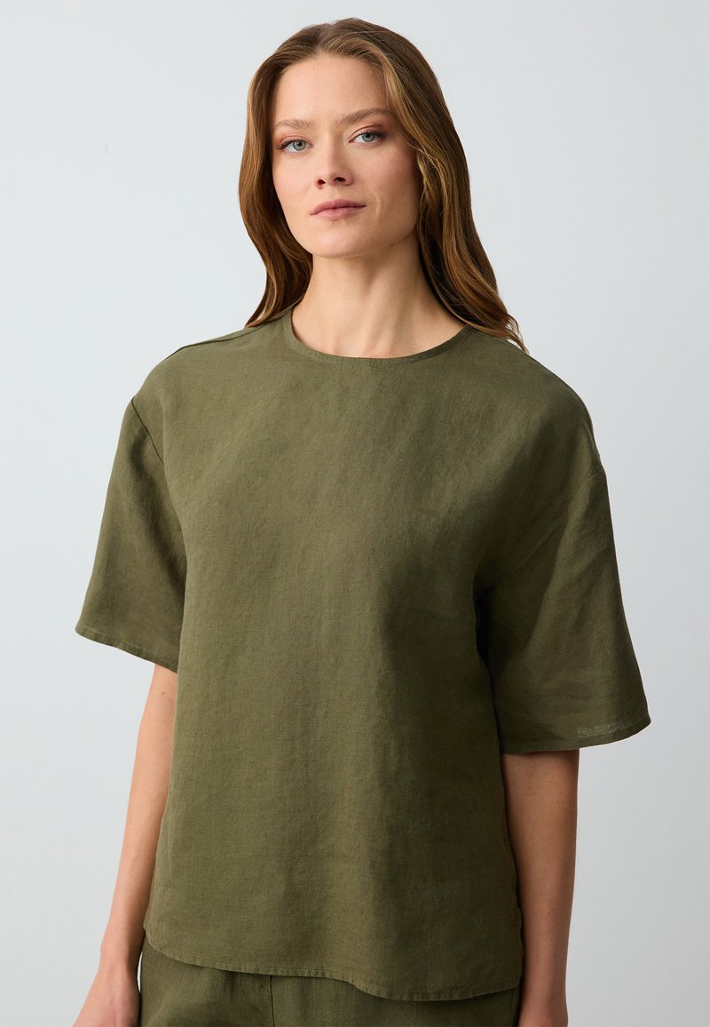 Camicetta corta in lino verde oliva con colletto rotondo e vestibilità comoda. Tessuto liscio e design minimalista senza decorazioni.
