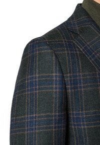 Wełniana marynarka w ciemnozielonym kolorze, z wzorem w kratę w odcieniach niebieskiego i brązowego. Wyróżniające się szczegóły to wyraźnie zarysowane ramiona oraz teksturowany materiał.