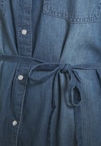 Denim kleita zila toņu gammā, ar pogām priekšpusē, divām krūšu kabatām un jostu viduklī, lai pielāgotu fit.