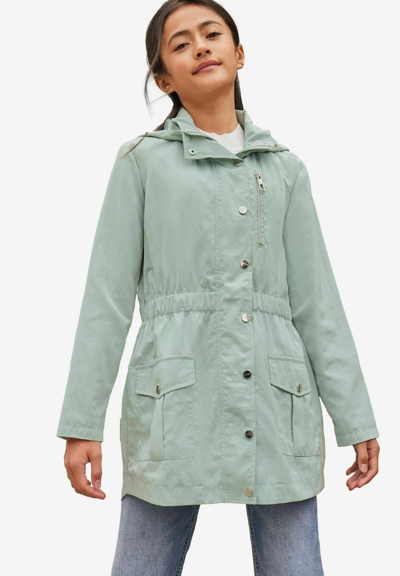 Lys grøn vandtæt jakke med hætte, elastisk talje, trykknapper og to frontlommer. Glat tekstur, afslappet design.