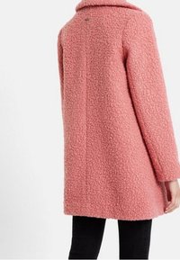 Fuzzy roze jas met een gestructureerd oppervlak en een notch kraag, met een rechte snit en achterkantnaaddetail, gedragen over zwarte broek.