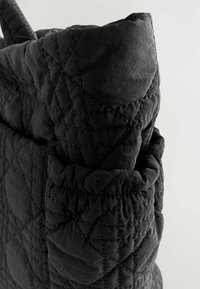 Schwarzer, gesteppten Stoff mit diagonaler Naht verfügt über einen gerafften Rand und eine Seitentasche, die einen strukturierten, schichtartigen Look kreiert.