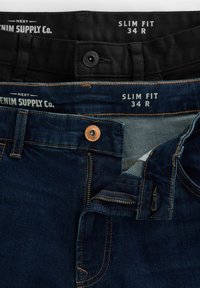 Twee paren slim fit jeans, één in donkerblauwe denim met koperen hardware en één in zwarte stof, beide maat 34 R.