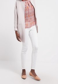 Ljust rosa strukturerad lång jacka, mönstrad blus i orange och lila, vita skinny jeans, persikofärgade ballerina med hjärtformade detaljer.