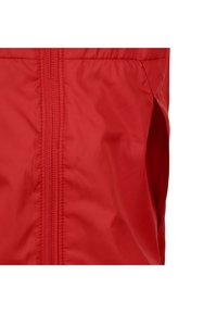 Giacca in nylon rossa con zip frontale, lati elasticizzati e superficie liscia. Il design include una vita leggermente arricciata per una migliore vestibilità.