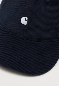 Gorra de pana azul oscuro con visera curvada y un pequeño logotipo de ojo bordado en blanco en el panel frontal.
