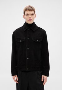 Melna džinsa jaka ar smailu apkakli, priekšējām kabatām un pogu aizdari. Raksturo kontrastējošas šuves un zamšāda līdzīgu tekstūru.