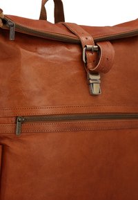 Braune Ledertasche mit oberem Reißverschluss, Metall-Gurtschnallenverschluss, vorderer horizontaler Reißverschlusstasche und einem Stoffgriff.