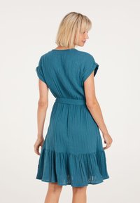 Teal, knielang jurk met een uitlopende zoom, mouwloos ontwerp en een geplooide tailleband. Gemaakt van textiel met een gestructureerde stof en verticale strepen.