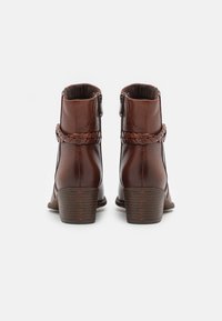 Bottes en cuir marron jusqu'à la cheville avec un détail en sangle tressée, bout rond et talon empilé. Fermeture éclair sur le côté. Texture lisse.
