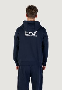 Marineblauer Hoodie mit entspannter Passform, der ein großes weißes Logo auf der Rückseite aufweist. Der Stoff wirkt glatt und hat eine weiche Textur.