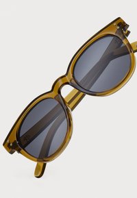 Round sunglasses with a translucent amber frame, grey tinted lenses, and straight arms. Features subtle silver accents near the temples.