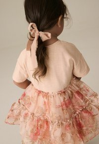 Bluse mit kurzen Ärmeln in blassrosa und einem floral geschichteten Rock aus transparenter Stoff. Der Rock hat einen rüschigen Saum und verschiedene Rosenmuster.