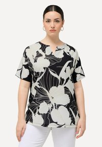 Sorte blomstret top med korte ærmer og V-udskæring, med hvide blomster omridset i beige på et glat stof.