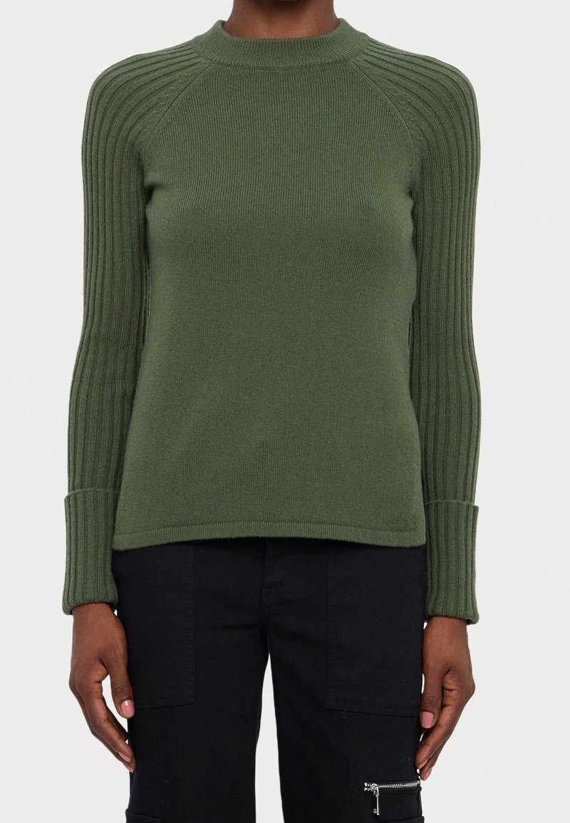 Pull vert tricoté avec un col rond, des détails côtelés sur les épaules et les manches, ainsi que des poignets ajustés, assorti à un pantalon cargo noir.