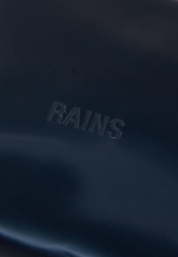 Temno modra vodoodporna tkanina z gladko teksturo; vsebuje vtisnjen logotip "RAINS" v subtilnem dizajnu.