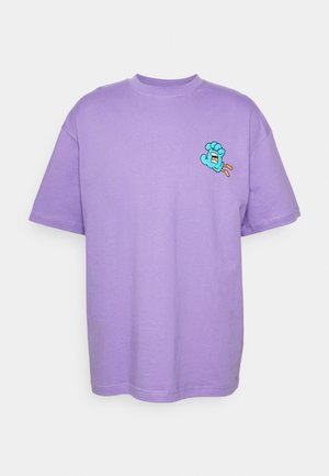 Lys lilla T-shirt med korte ærmer og lille blå tegneseriehånd-grafik nær venstre bryst, med åben mund og orange ben.