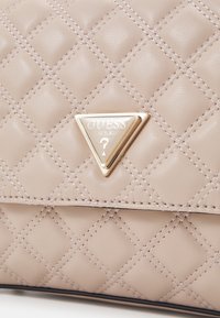 Borse a tracolla beige trapuntata con logo triangolare dorato, caratterizzata da sezioni imbottite e dettagli di cucitura fine, che offrono una superficie testurizzata.