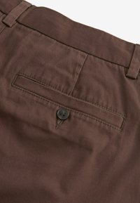 Brune stofbukser med en glat tekstur, der har en baglomme sikret med en mørk knap og en flad taljedesign.