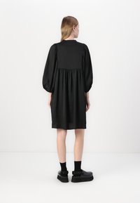Vestido preto com design de mangas bufantes, forma fluida e saia franzida. Estilo combinado com calçado preto robusto e meias até ao tornozelo.