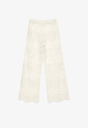 White crochet wide-leg pants featuring hexagonal patterns, scalloped edges, and an elastic waistband for an open, airy design.