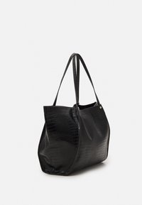 Musta kangaskassi, joka on valmistettu tekstuurillisesta synteettisestä nahasta krokotiilikuviolla. Kassissa on pitkät hihnat ja leveä avaus, mikä tekee pääsystä vaivatonta.