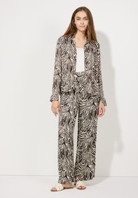 Zwart-wit zebra print pyjama set met lange broeken en een button-up shirt; gladde stof, relaxte pasvorm en wijde mouwen. Sandalen inbegrepen.