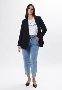 Sort dobbeltknappet blazer over en hvid grafisk t-shirt, parret med høj talje lyseblå jeans og sorte spidse pumps.