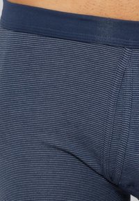 Laivastonsiniset raidalliset shortsit, joissa on pehmeä ja joustava kangas. Vyötäröllä on yksivärinen laivastonsininen resori. Pystysuorat raidat ovat hillittyjä ja tasaisesti sijoitettuja.