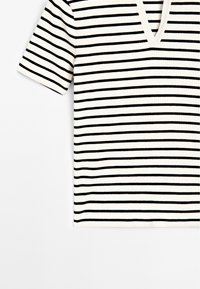 Chemise blanche à manches courtes côtelée avec des rayures horizontales noires et un col en V sur un fond clair.