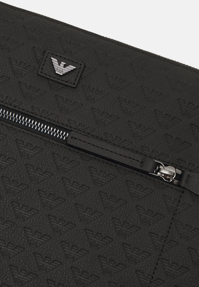 Black textured clutch bag featuring an embossed logo pattern, front zip closure, and a silver-tone hardware accent.