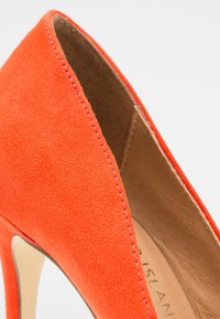 Chaussure à talon haut en suede orange avec un bout pointu et un design à découpe basse, présentant des détails de couture subtils le long du bord et un intérieur beige.