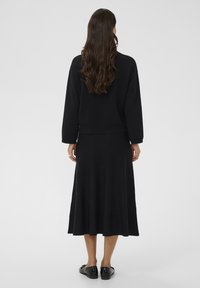 Crna pletena haljina s raširenom suknjom, dugim rukavima i skraćenim gornjim dijelom; meka tekstura i bezšavni dizajn bez vidljivih kopči.