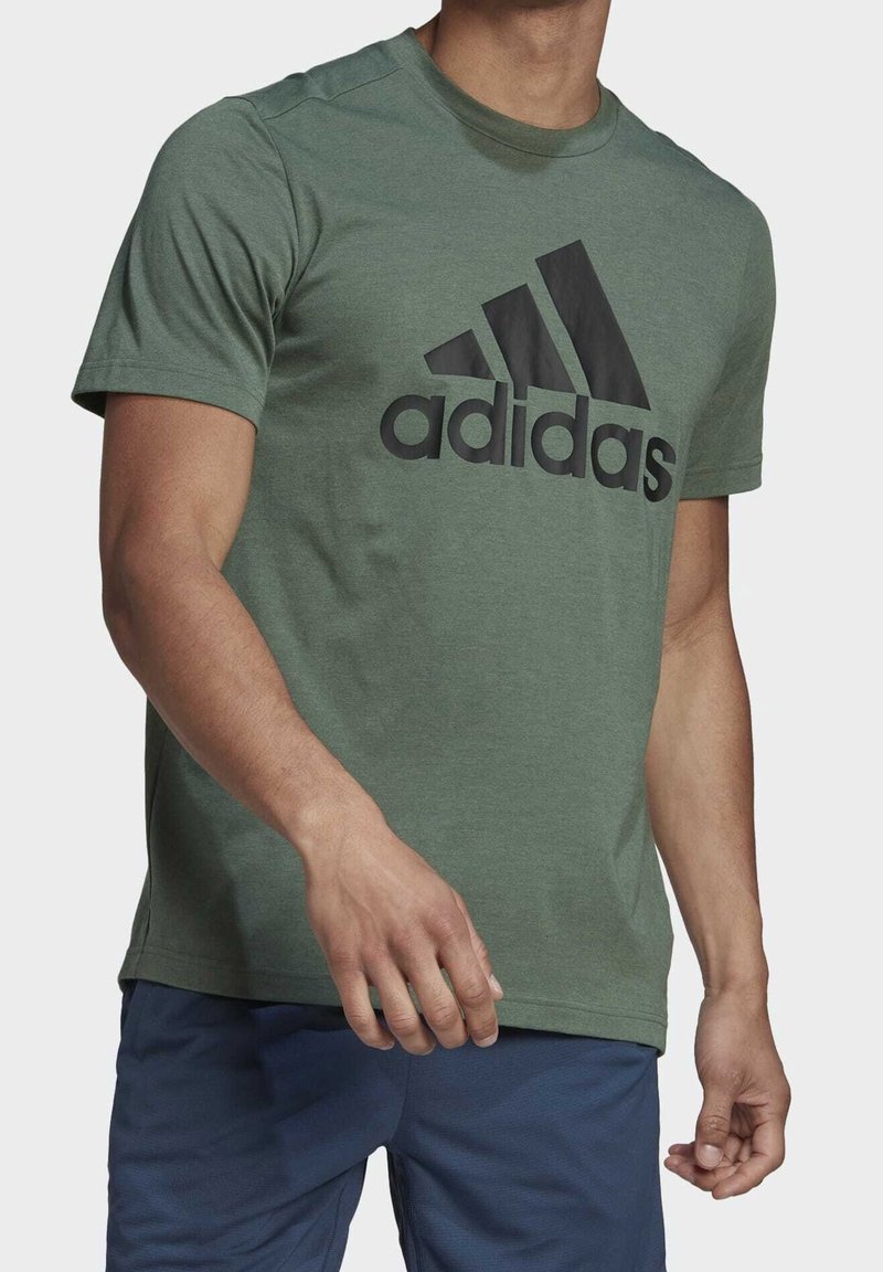 Grön bomullströja med rund halsringning, med en stor svart Adidas-logotyp framtill. Kortärmad, avslappnad passform, minimal struktur.