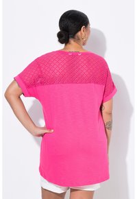 Růžové tričko s krajkovým vzorem na vršku a pevným materiálem dole, krátké rukávy a uvolněný střih.