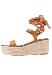 Bruna lädersandaler med kilklack och en plattform med repstruktur samt korsade ankle straps. Släta remmar och ett platt tåband för komfort.