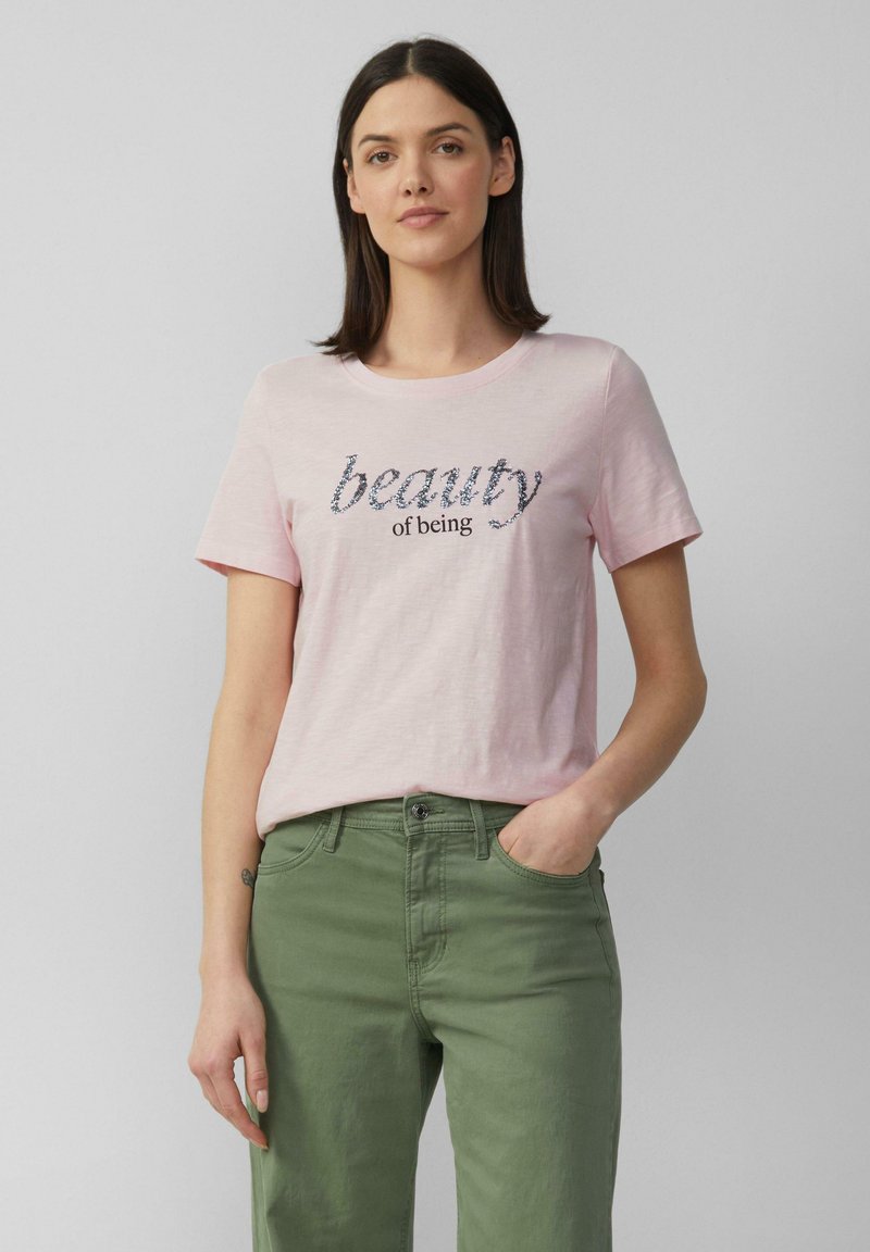 T-shirt rose clair à manches courtes avec une broderie texturée portant l'inscription "la beauté d'être". Assorti à un pantalon vert, offrant une coupe décontractée.