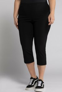 Pantaloni capri neri con un design aderente, realizzati in tessuto elasticizzato. Presentano una vita media e una texture liscia. Abbinati a sneakers nere.