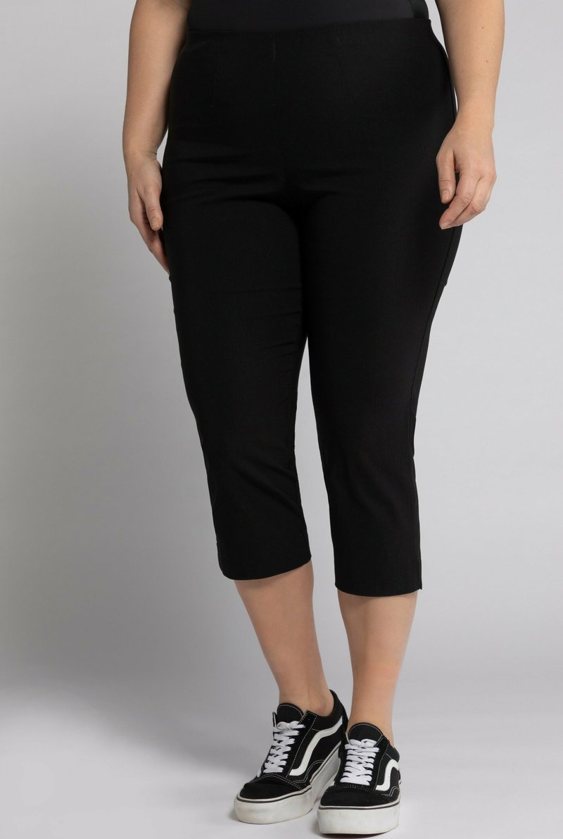 Pantaloni capri neri con un design aderente, realizzati in tessuto elasticizzato. Presentano una vita media e una texture liscia. Abbinati a sneakers nere.