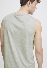 Grijze mouwloze t-shirt met een iets losse pasvorm, gemaakt van zachte, gestructureerde stof; toont de achterkant en een ronde halslijn. Geen zichtbare patronen.