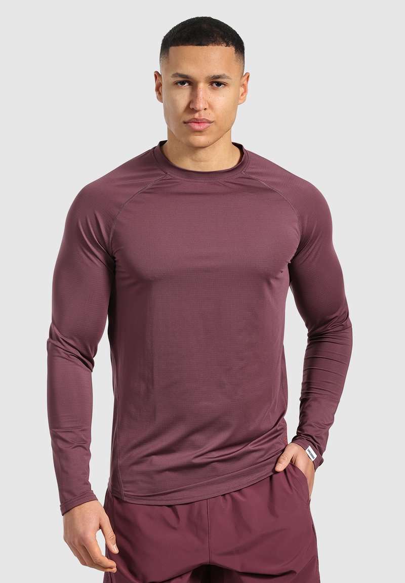 Maglietta sportiva a maniche lunghe di un marrone scuro, realizzata in un tessuto liscio e elasticizzato con maniche raglan e una silhouette aderente.
