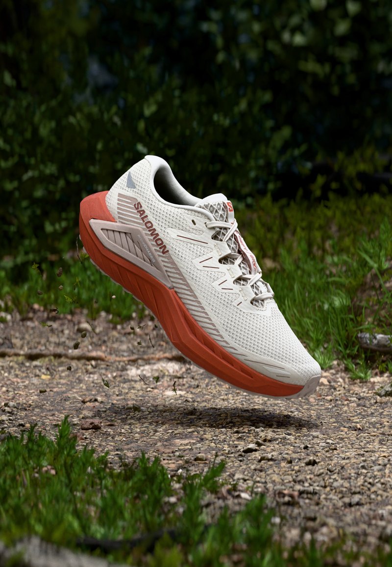 Juoksukenkä, jossa valkoinen verkkopäällinen ja oranssi välipohja. Varustettu kuvioidulla pohjalla ja näkyvällä tuotemerkin logolla sivulla.