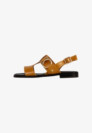 Lædersandal i en gulbrun farve med åben tå, rund metalaccent, justerbar ankelrem og flad sort sål.
