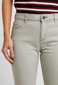 Jeans in cotone grigio chiaro con un design a cinque tasche, chiusura con bottone e vestibilità slim. Il tessuto ha una superficie liscia e dettagli di cucitura discreti.