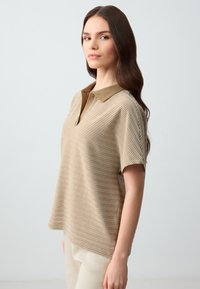 Polo a righe in beige e marrone, con colletto solidale, maniche corte e vestibilità rilassata. Una texture sottile aggiunge profondità al design.